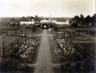 Greenhouse complex and gardens with power plant smokestack in background