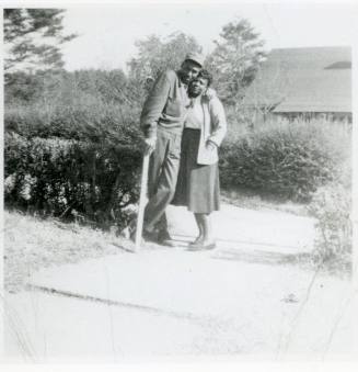 J.D. Spease and Betty Ruth Warren standing in opening of low hedge at the foot of a paved walk, ...